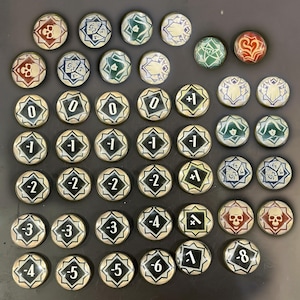 Puede incluir: Una colección de fichas de juego redondas con varios diseños y números. Las fichas presentan símbolos como calaveras, dados y patrones geométricos. Los números varían de -8 a +1. Las fichas tienen un borde dorado metálico y están sobre un fondo oscuro.