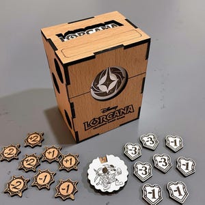 May include: Wooden card game box with the text "LORCANA TRADING CARD GAME". Includes wooden tokens with numbers and a circular token with a cartoon character. The box has a lid and a circular design.