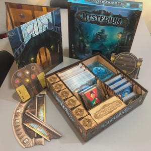 Pode incluir: O jogo de tabuleiro "Mysterium" é exibido, com uma caixa com uma ilustração de uma casa assombrada. O jogo inclui cartas, componentes de madeira e um tabuleiro com uma ponte e um design de vitral. O jogo está em uma superfície cinza.
