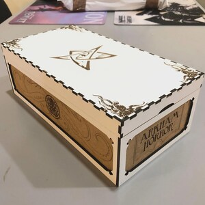 A white wooden box with a decorative design on the lid, sitting on a table.