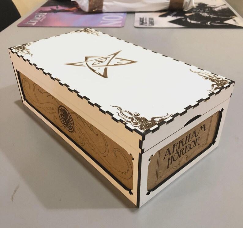 A white wooden box with a decorative design on the lid, sitting on a table.