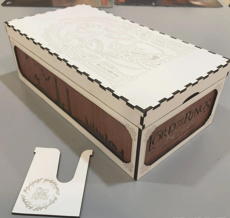 A wooden box with a lid and a cutout on the side, featuring the Lord of the Rings logo and text.