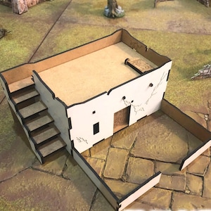 May include: A miniature white building with a flat roof, stairs, and a small door. The building has a rectangular shape with black trim and is designed for tabletop gaming or model building.