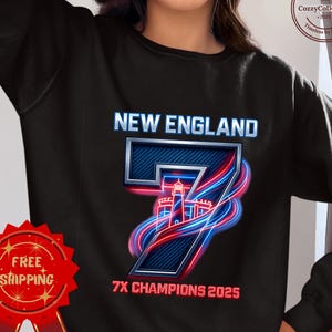 May include: Black sweatshirt featuring the text "NEW ENGLAND" above a large number "7" with a lighthouse graphic. The number is outlined in blue and red neon. The text "7X CHAMPIONS 2025" is below the number.