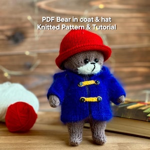 Puede incluir: Un oso de peluche tejido con un sombrero rojo y un abrigo azul con botones amarillos. El oso tiene un hocico blanco y está sobre una superficie de madera. El texto "PDF Bear in coat & hat Knitted Pattern & Tutorial" es visible.