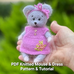 Könnte beinhalten: Eine handgestrickte, graue Maus, die ein rosa Kleid mit einem floralen Design und zwei goldenen Knöpfen trägt. Die Maus hat ein rosa Stirnband und eine Schleife. Der Text "PDF Knitted Mouse & Dress Pattern & Tutorial" befindet sich unten.