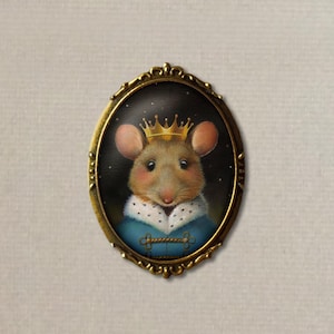 May include: A gold-toned oval brooch with a detailed design. The brooch features a painted image of a mouse wearing a gold crown and a blue and white coat against a dark background with white stars.