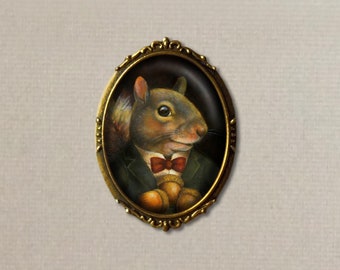 May include: A vintage-style oval brooch featuring a painted portrait of a squirrel wearing a bow tie and holding acorns. The brooch has a gold-toned metal frame with ornate details.