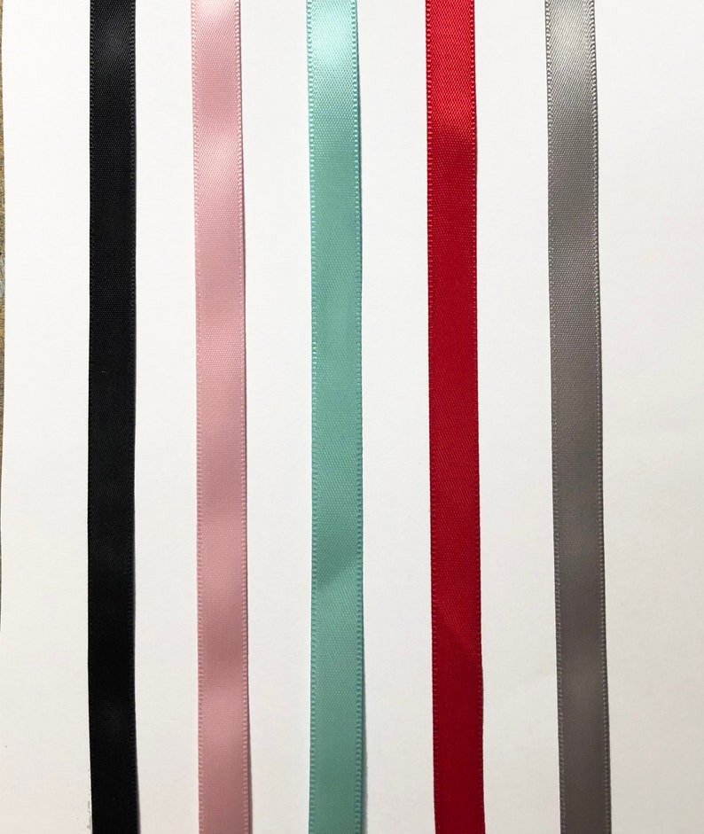 Peut inclure: Assortiment de six bobines de ruban satin&eacute; de diff&eacute;rentes couleurs, dont noir, rose, bleu clair, rouge et gris.