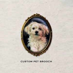 Peut inclure: Une broche personnalis&eacute;e pour animal de compagnie repr&eacute;sentant un chien blanc aux yeux bruns dans un cadre ovale dor&eacute;. La broche est un excellent moyen de se souvenir de votre ami &agrave; fourrure.