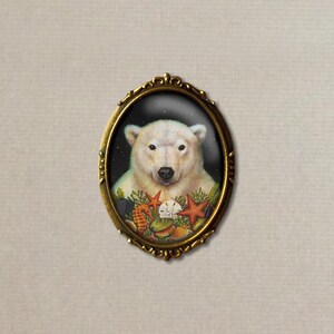 May include: A white polar bear with a black nose and eyes is surrounded by seashells and starfish in a gold oval frame. The background is a dark blue.