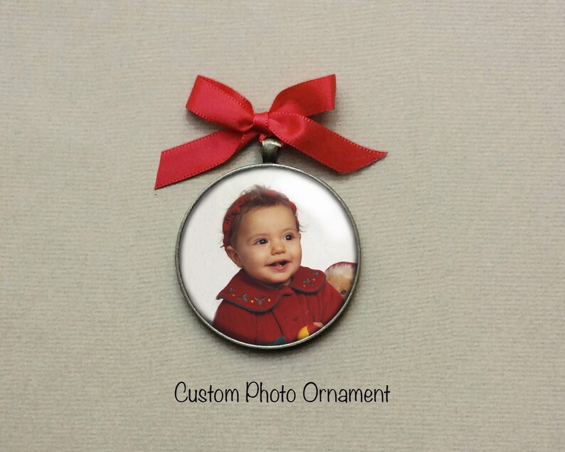 Peut inclure: Une d&eacute;coration ronde en argent avec un ruban rouge. La d&eacute;coration pr&eacute;sente une photo d'une petite fille portant un manteau rouge et un bandeau rouge. Le texte "Custom Photo Ornament" est imprim&eacute; sous la d&eacute;coration.