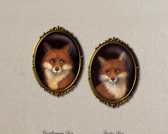 May include: Two oval-shaped brooches with a gold-toned frame and a glass cameo featuring a red fox with white fur on its chest and neck. The fox is looking directly at the viewer.
