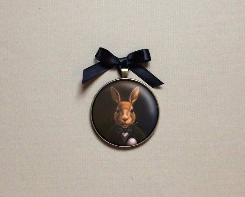 This mysterious rabbit ornament will add a touch of Victorian charm to your decor. 2" round bronze setting with a gold hanging cord and black satin bow.