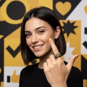 Può includere: Un anello nero con la scritta "ANCHE SI" in lettere dorate. L'anello è indossato su un dito. Lo sfondo è giallo e nero con varie forme.