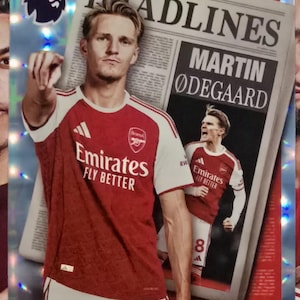 Puede incluir: Una tarjeta coleccionable Topps de la Premier League con Martin Ødegaard con la camiseta del Arsenal. La tarjeta tiene un fondo de estilo periódico con el titular "HEADLINES" y el nombre del jugador. El logotipo del Arsenal y "Emirates FLY BETTER" son visibles.