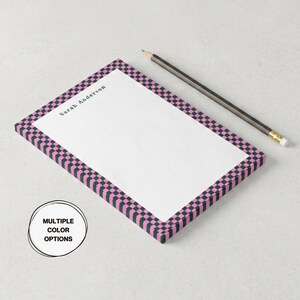 May include: A rectangular notepad with a pink and black checkered border and the name "Sarah Anderson" printed at the top. A pencil rests on the side. The notepad has a white interior and the words "MULTIPLE COLOR OPTIONS" are in a circle.