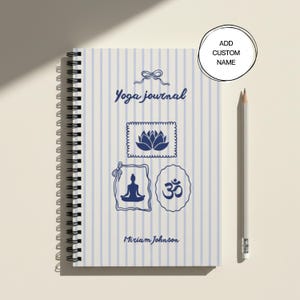 Könnte beinhalten: Ein spiralgebundenes Yoga-Journal mit hellblau-weiß gestreiftem Einband. Der Einband zeigt eine dunkelblaue Schleife, den Text "Yoga journal", eine Lotusblüte, eine Person in Yoga-Sitzhaltung, ein Om-Symbol und den Namen "Miriam Johnson".