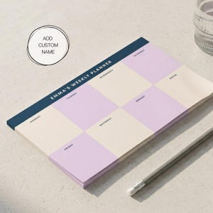Pode incluir: Um bloco de notas de planeamento semanal com uma borda azul marinho e o texto "EMMA'S WEEKLY PLANNER". O planejador apresenta uma grade com quadrados em lavanda e creme. Um lápis está sobre a superfície.