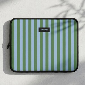 Peut inclure: Une housse pour ordinateur portable à rayures vertes, bleu clair et blanches. La housse a une bordure noire et une fermeture éclair noire. Le nom "SARAH" est imprimé sur un rectangle noir au centre.