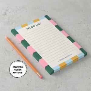 May include: A rectangular notepad with a white lined interior, the text TO DO LIST at the top, and the name MADISON ANDERSON at the bottom. The border features a repeating pattern of pink, dark green, yellow, and light blue squares. An orange pencil lies beside it, and a circular graphic reads MULTIPLE COLOR OPTIONS.