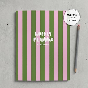 May include: A weekly planner with vertical pink and olive green stripes. The cover features the white text "WEEKLY PLANNER" and "EMMA JONES" in the centre. A grey pencil is positioned to the right of the planner, and a circular badge in the top right corner contains the text "MULTIPLE COLOR OPTIONS".