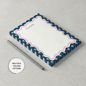 May include: A rectangular notepad with a navy blue floral pattern border and a scalloped lavender frame. The notepad has the name "Charlotte" printed in green. A gray pencil rests beside the notepad. The image also includes a circle with the text "MULTIPLE COLORS OPTIONS".