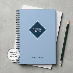 Könnte beinhalten: Ein hellblaues Notizbuch mit Spiralbindung und einem dunkelblauen rautenförmigen Emblem mit dem weißen Text NOTES & IDEAS sowie dem Namen MIRIAM BROWN darunter. Ein dunkelgrüner Stift liegt rechts neben dem Notizbuch auf einer grauen Fläche.