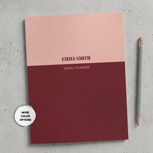 May include: A weekly planner with a two-tone design featuring a light pink top section and a dark maroon bottom section. The text EMMA SMITH is printed in dark maroon, followed by the text WEEKLY PLANNER. A gray pencil lies to the right.