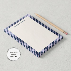 May include: A rectangular notepad with a checkered border in navy blue and lavender. The notepad has the name "MADISON JONES" printed at the top and includes a wooden pencil with a pink eraser. The image also includes a circular graphic that says "MULTIPLE COLOR OPTIONS."