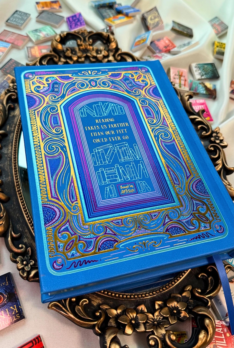 May include: A blue book with gold and purple decorative accents and the text "Reading takes us farther than our feet could ever go." The book is surrounded by other miniature books.