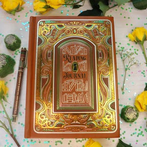 May include: A brown Reading Journal with gold and green detailing, inscribed with "Reading Journal". A pen lies nearby, with yellow roses and foliage. The journal is surrounded by yellow roses and greenery.