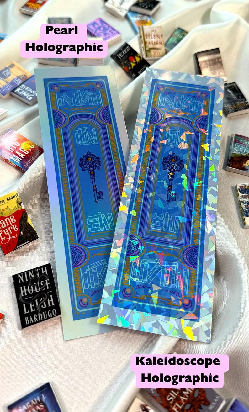 May include: Two holographic bookmarks with a blue door design and a key in the center. The text "NIKA" is visible. The bookmarks are surrounded by miniature books. The text "Pearl Holographic" and "Kaleidoscope Holographic" are also visible.