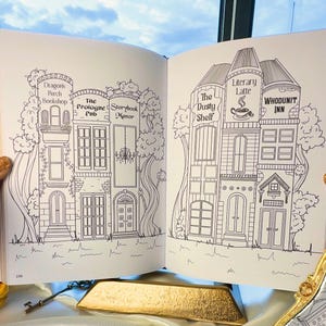 May include: Open book with detailed line drawings of whimsical buildings, including a bookshop, pub, and inn. The text on the pen reads "IT'S A GOOD DAY TO HAVE A GOOD DAY". A key and gold bar are also visible.