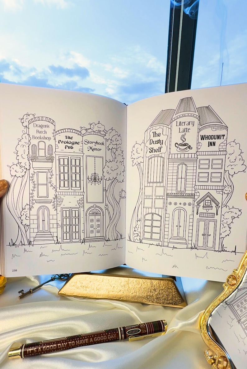 May include: Open book with detailed line drawings of whimsical buildings, including a bookshop, pub, and inn. The text on the pen reads "IT'S A GOOD DAY TO HAVE A GOOD DAY". A key and gold bar are also visible.