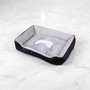 Puede incluir: Una cama rectangular para mascotas con exterior negro e interior gris. La cama tiene un diseño de huella de pata blanca en el centro. La cama está diseñada para perros o gatos pequeños y medianos.