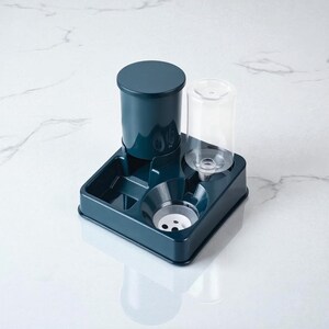 May include: A teal pet feeder and water dispenser. The unit has a cylindrical food container, a clear water bottle, and a square base with feeding bowls. The design is modern and compact, suitable for small pets.
