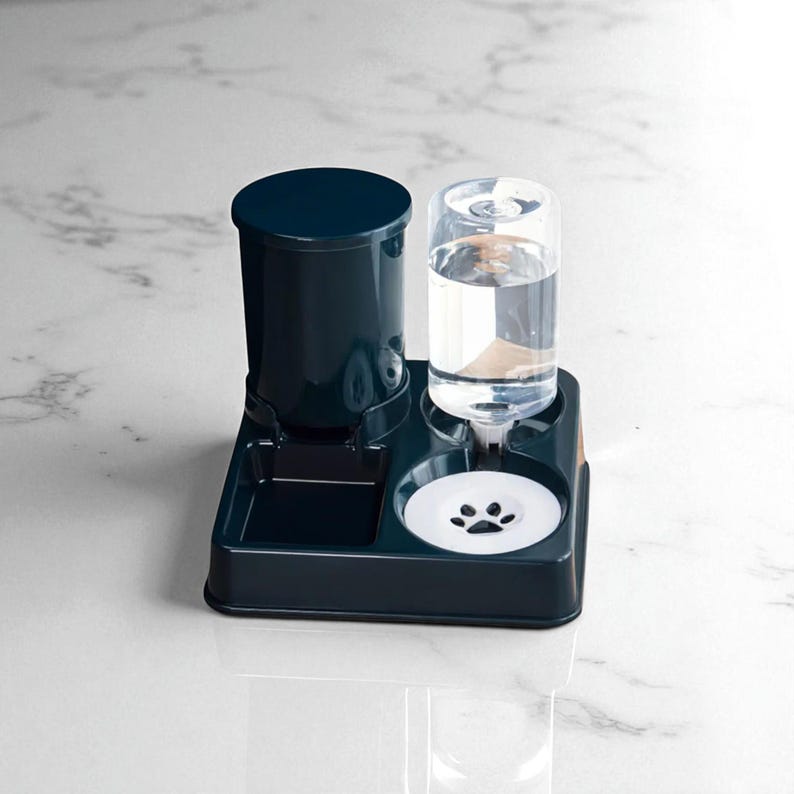 May include: A dark teal pet feeder and waterer. The waterer has a clear, cylindrical water bottle. The feeder has a dark teal container with a lid. The base has a small food tray and a white paw print design.