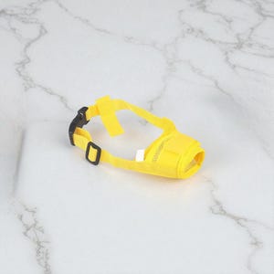 May include: A yellow dog muzzle with adjustable straps and a black buckle. The muzzle features a mesh front for breathability and is designed to fit around a dog's snout.