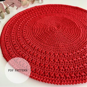 May include: A bright red, circular crochet doily. The handmade item features concentric circles of textured stitches, with a detailed edge. The text "PDF PATTERN" is visible in a white circle. Ideal for home decor.