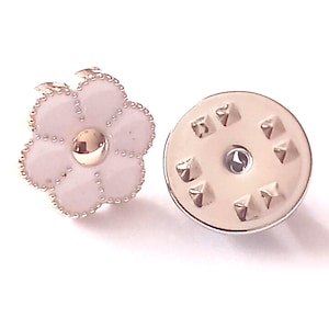 Puede incluir: Un broche en forma de flor con acabado esmaltado blanco y detalles dorados. El broche tiene un centro dorado y un borde detallado. La parte posterior del broche tiene un cierre metálico. Accesorio decorativo.