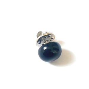 May include: A dark navy blue lapel pin with a rounded, polished stone design. The pin has a silver-colored backing with a clasp. The pin is set against a white background.