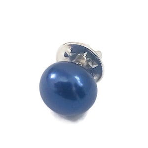 May include: A navy blue lapel pin with a shiny, round, pearl-like design. The pin has a silver-colored backing and a classic, elegant appearance. The pin is set against a white background.