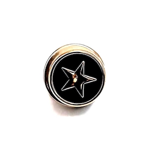 May include: A gold-colored metal button with a black center featuring a white star design. The button has a circular shape with a raised edge. The star is outlined in white, creating a contrast against the black background.