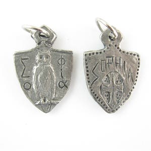 May include: A silver pendant in the shape of a shield with an owl and Greek letters on one side and the word "SOPHIA" on the other side.