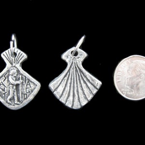 May include: Two silver pendants, one with a scallop shell design and the other with a figure of a person, are shown next to a US dime for size comparison.