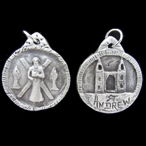 May include: Silver pendant with two sides. One side features a depiction of Saint Andrew with a cross and two fish. The other side features a building with the text "St Andrew".