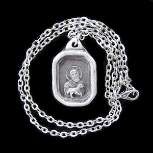 May include: A silver chain necklace with a silver pendant featuring a relief image of Saint Francis of Assisi holding a lamb.
