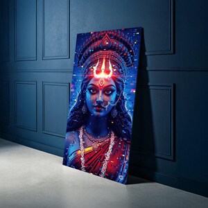 May include: A digital art print of a woman with a red bindi and a trident above her head. The artwork features a vibrant colour palette of red, blue, and purple. The woman is adorned with jewellery and a red sari. The print is leaning against a dark blue wall.
