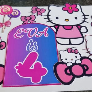 May include: A sheet of Hello Kitty-themed birthday decorations. The design includes multiple Hello Kitty figures, pink bows, lollipops, and the text "EVA is 4" in a gradient of pink and purple. The decorations are on a white background.